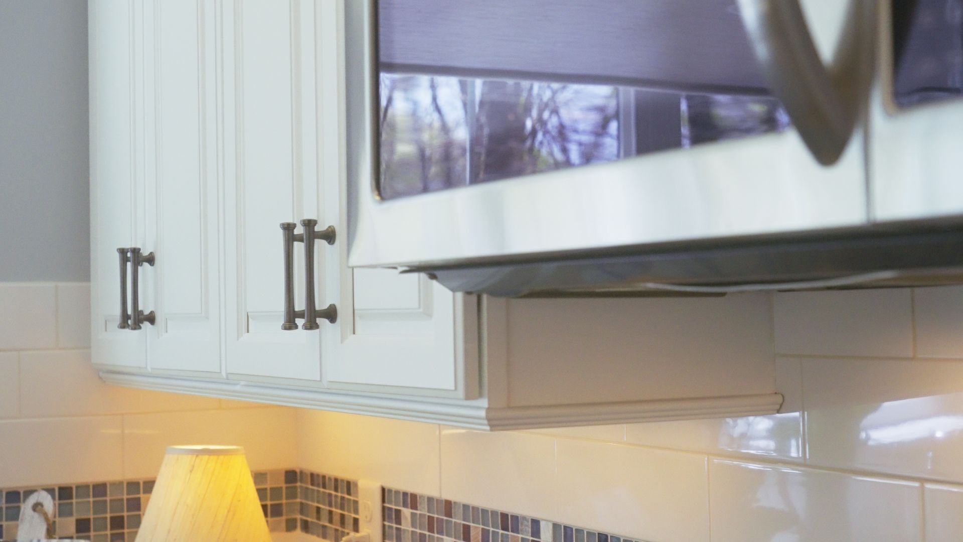 White kitchen cabinets and a microwave above a tile backsplash. A lamp glows on the counter.