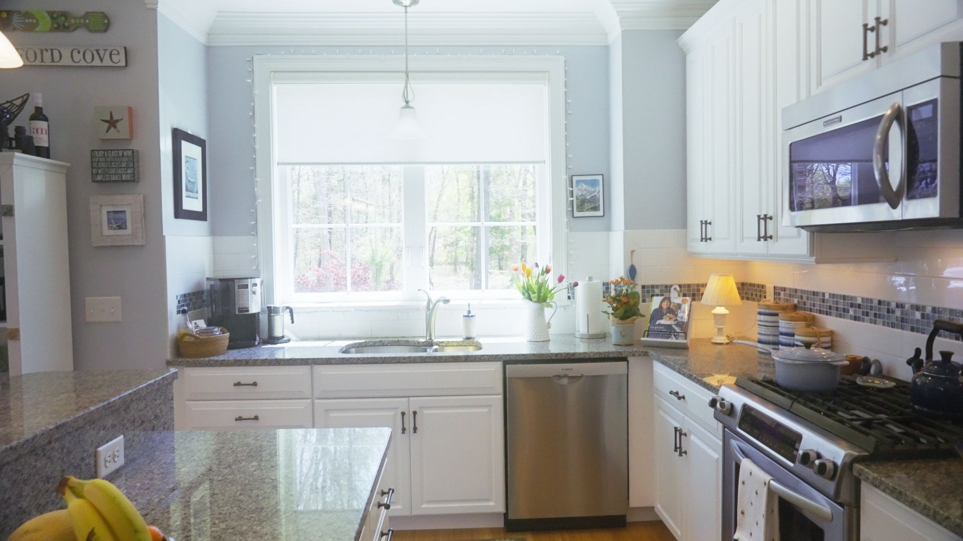 White kitchen with stainless steel appliances, a large window, and granite countertops.