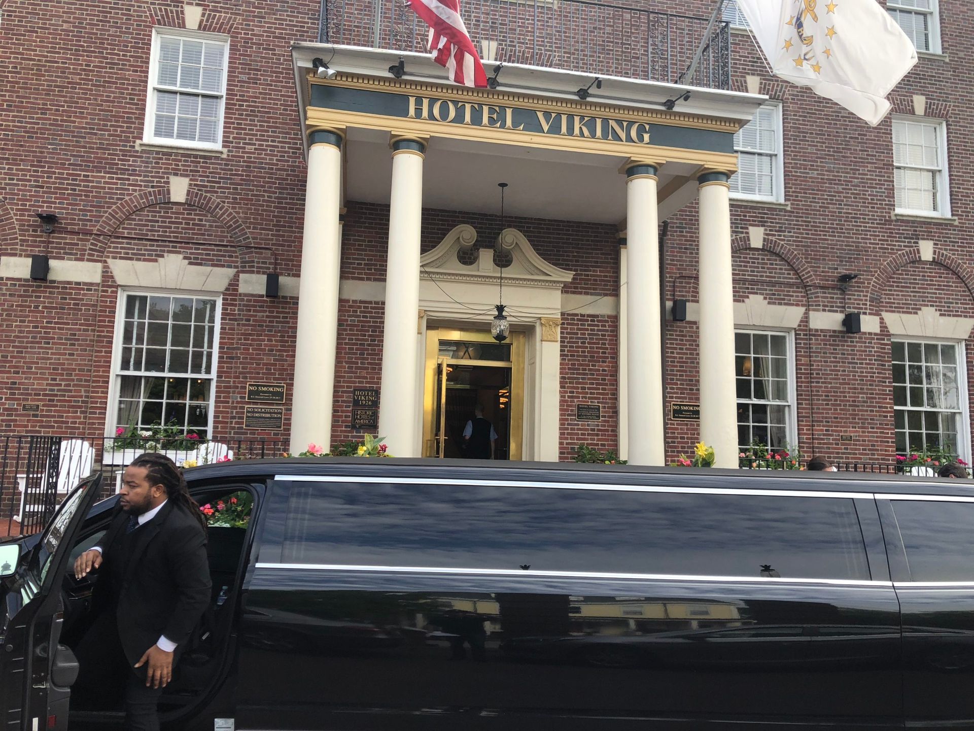 A black limousine in front of the Hotel Viking with a person in a suit exiting the vehicle. Red brick building with white columns.