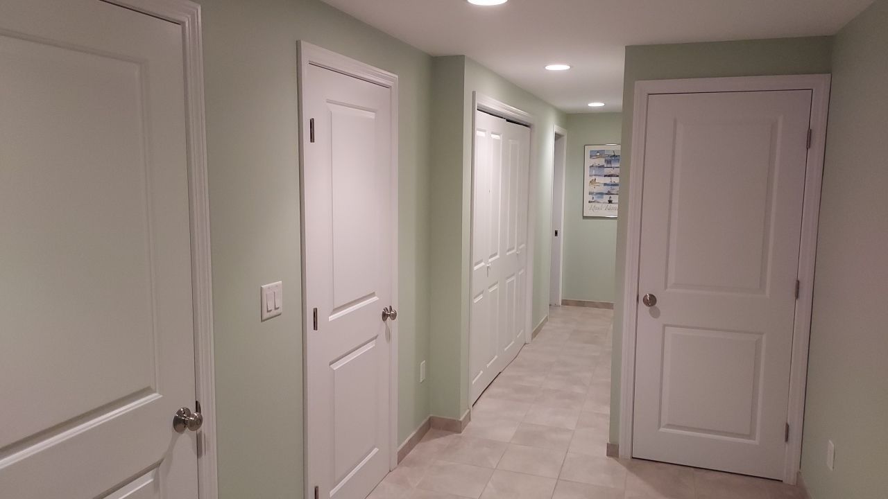 Hallway with light green walls, white doors, and beige tile flooring. Recessed lighting illuminates the space.