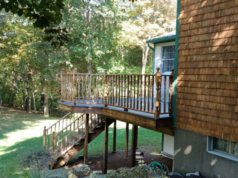 Wooden deck attached to a house with stairs leading down to a grassy backyard. The house has brown shingle siding.