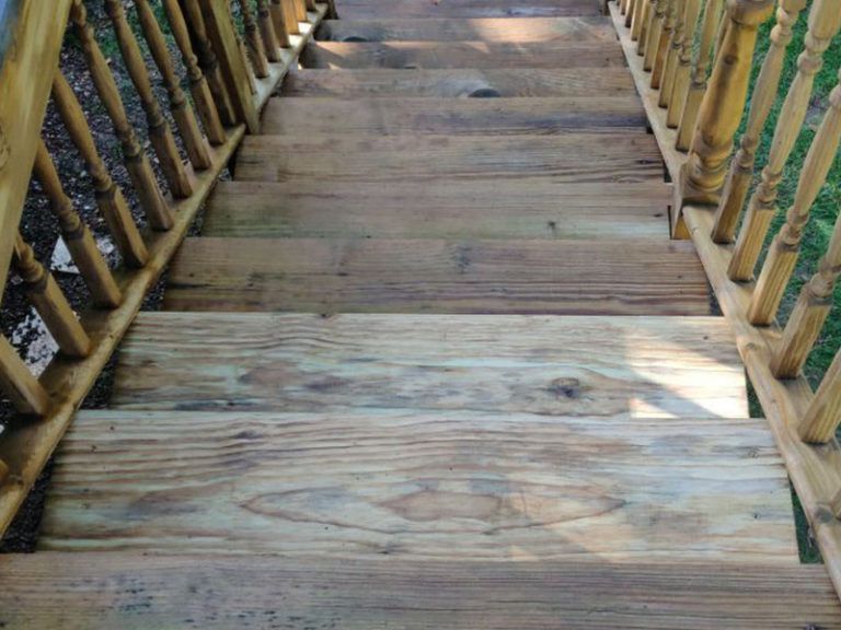 Wooden outdoor staircase with railings, viewed from above. The steps appear weathered and worn.