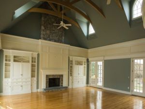 Empty living room with hardwood floors, fireplace, built-in cabinets, and arched ceiling. Green walls, white trim, and a ceiling fan.