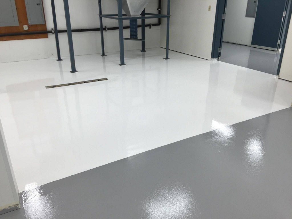 A room with a glossy, two-tone floor, white and gray. Metal supports and a dark doorway are visible.
