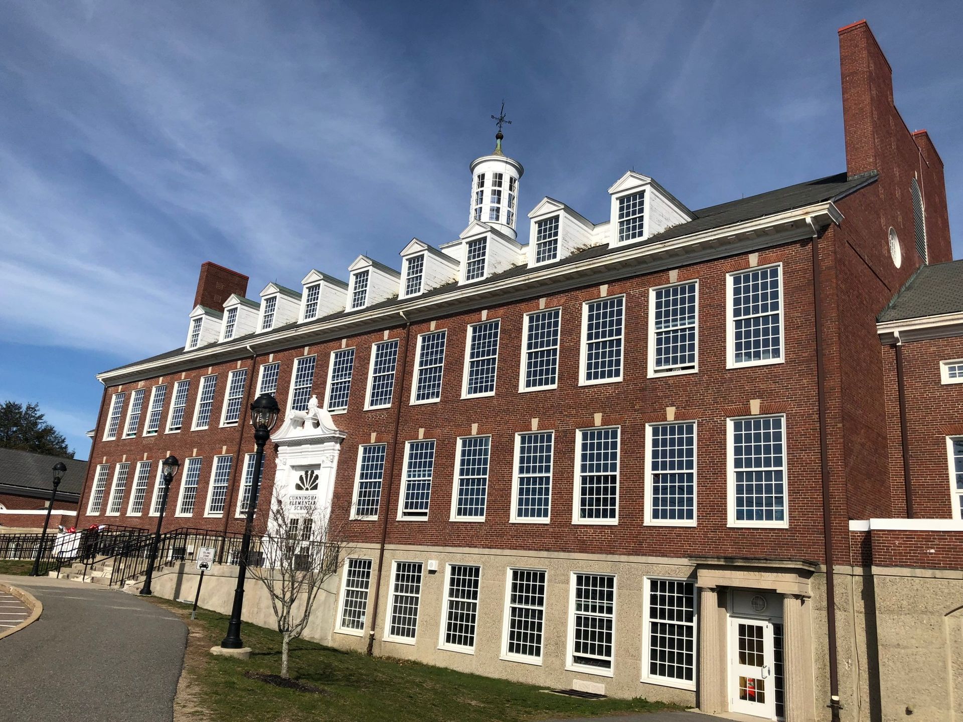 Red brick building with white-trimmed windows and a small cupola on top. Daytime, clear sky.
