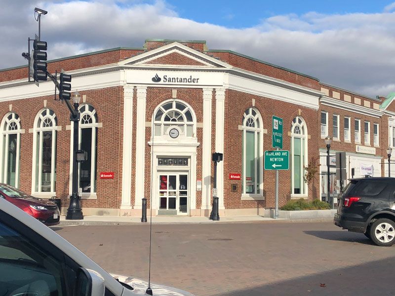 A Santander bank building made of red brick sits on a street corner with traffic lights and passing cars.