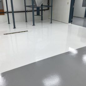 A shiny white and gray epoxy floor in a commercial space.  Metal support beams and industrial equipment are visible in the background.