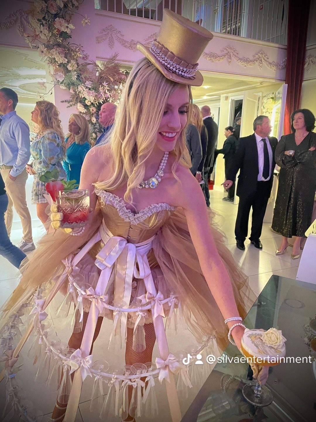 Vrouw in gouden korsetjurk en hoed biedt eten aan tijdens evenement.