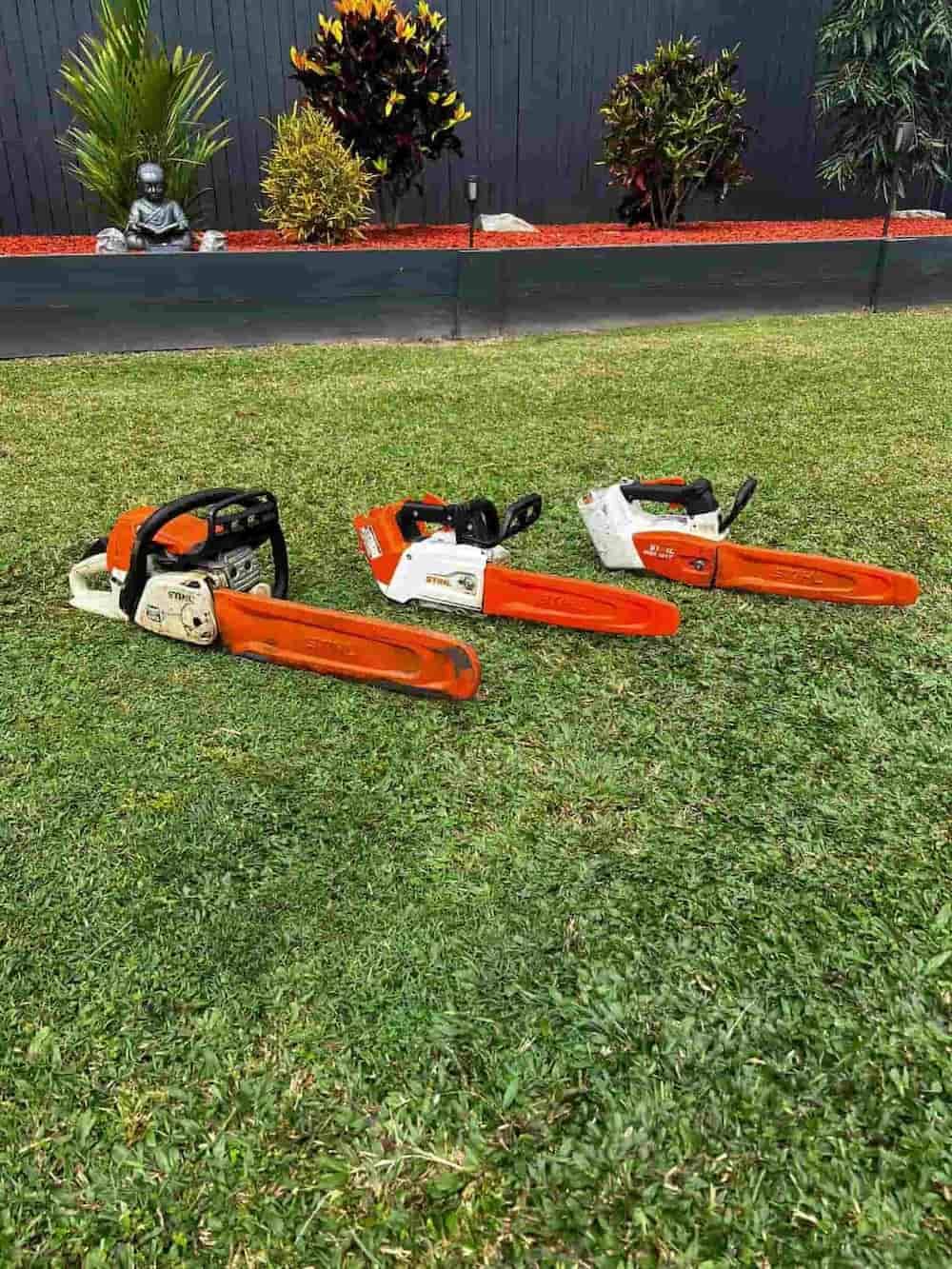 Three Chainsaws With Orange Bars on Green Grass — Mow & Mulch Lawn & Garden Maintenance In White Rock, QLD