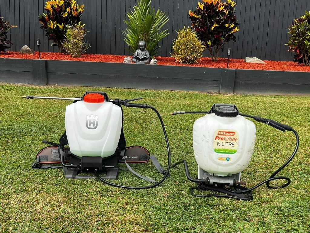 Two White Backpack Sprayers on Grass Against a Fence With Plants — Mow & Mulch Lawn & Garden Maintenance In White Rock, QLD