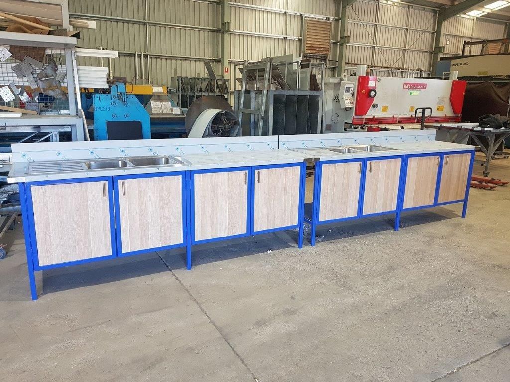 A row of wooden cabinets with stainless steel sinks in a factory.