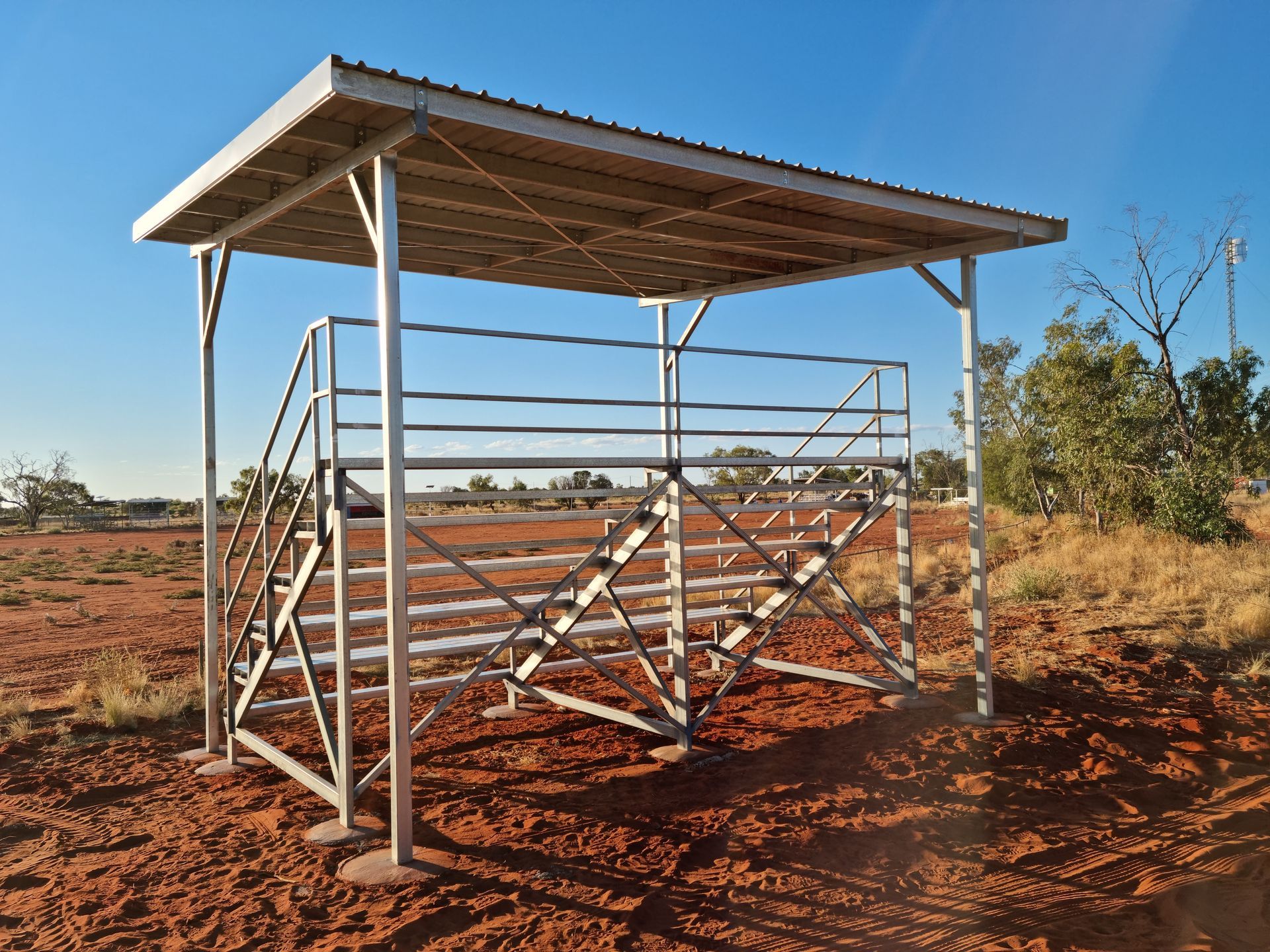 A metal structure with stairs and a roof in the middle of a dirt field.