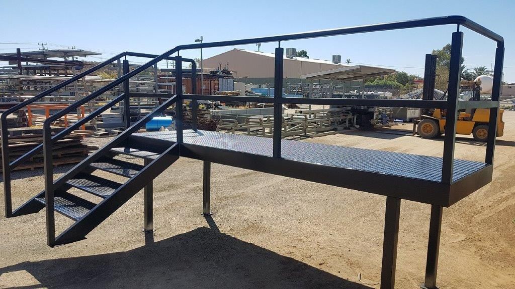 A metal platform with stairs and a railing in a dirt field
