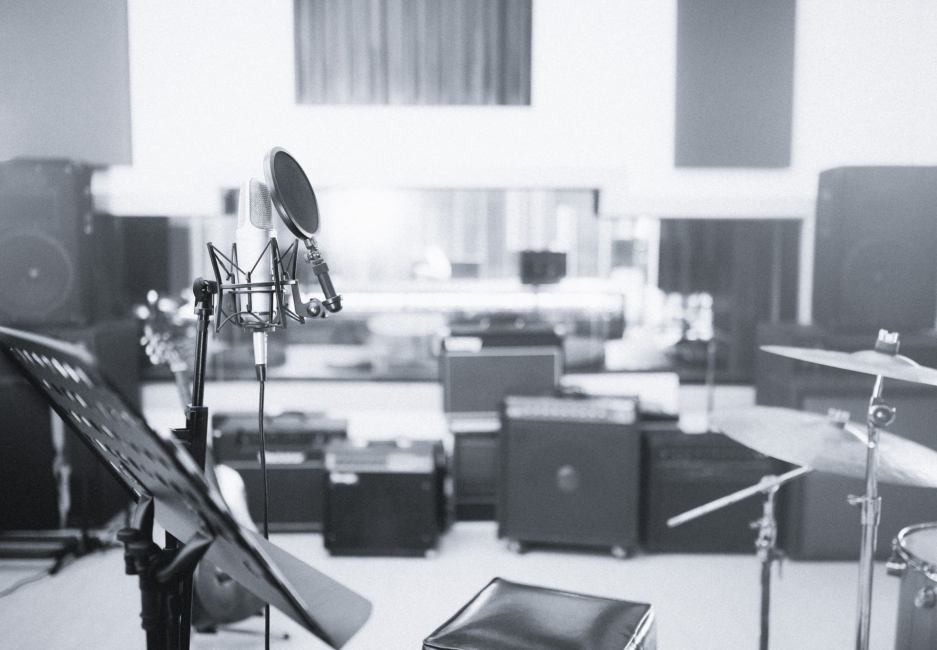 Microphone and music stand in recording studio, with drums and amplifiers visible in the background.
