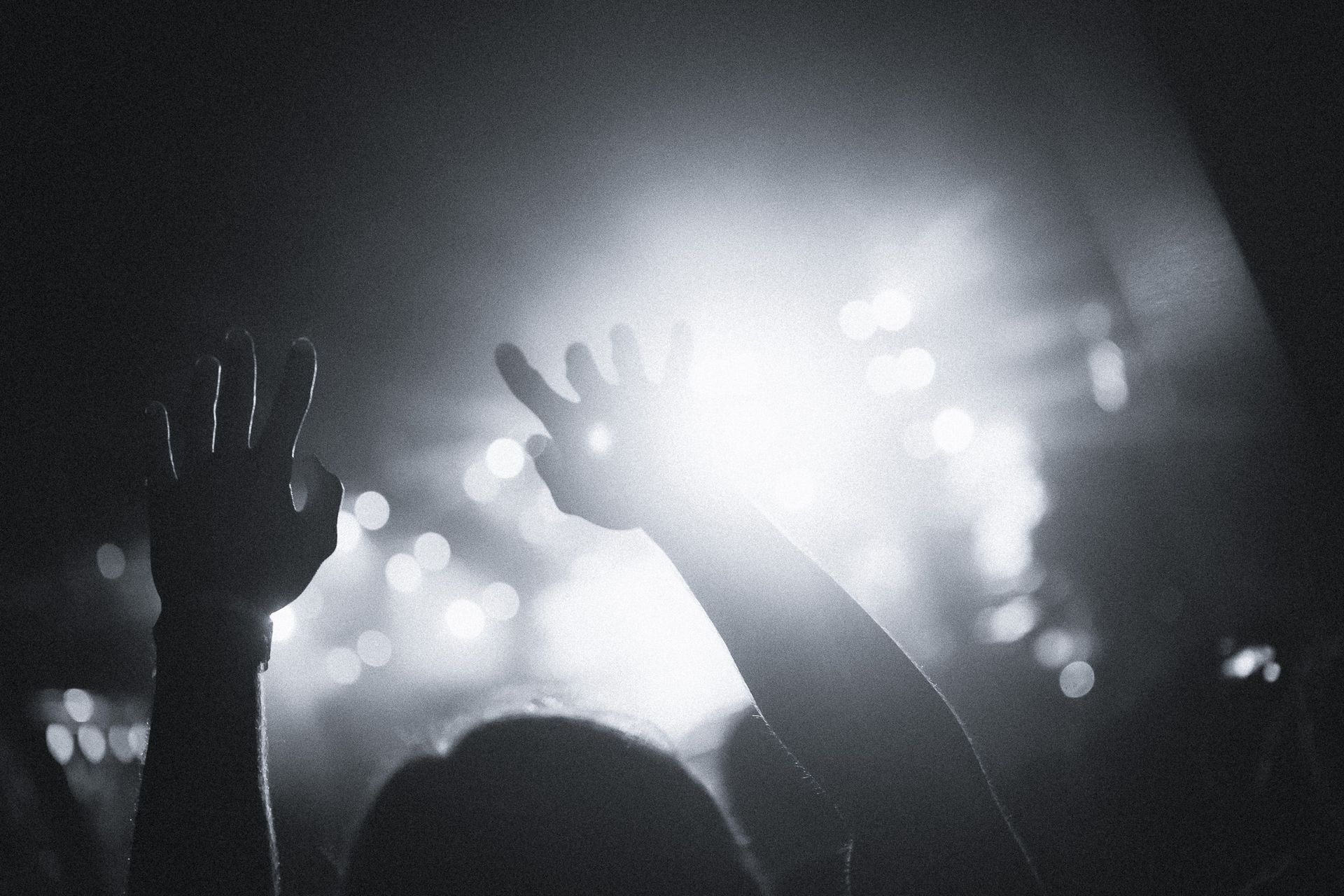 Worship concert scene with raised hands silhouetted against bright stage lights.