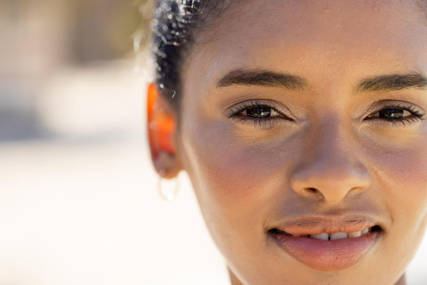 Close-up portrait of a person with dark hair, glowing skin, and a soft, gentle smile, illuminated by natural light.