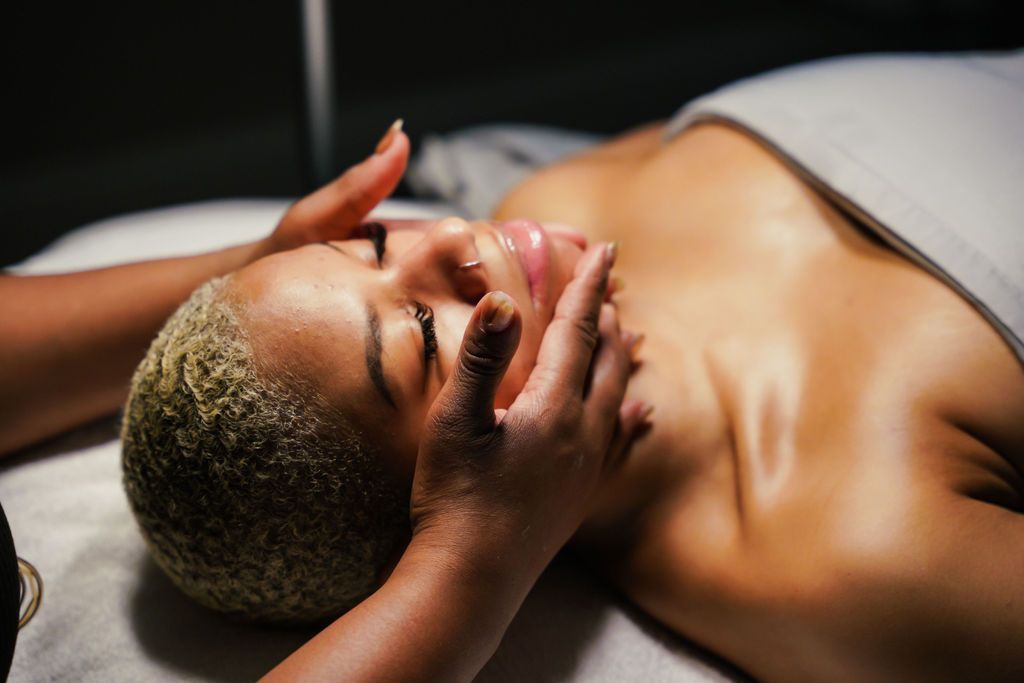 Woman receiving facial massage in spa. Light skin, blonde hair, dark room.