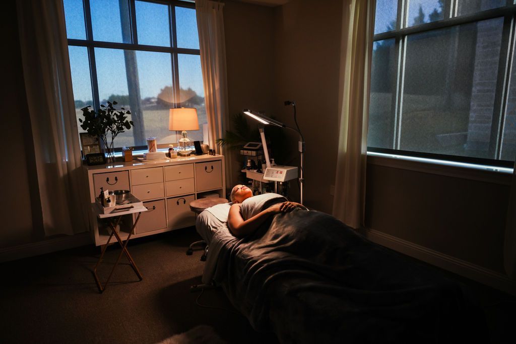 A person is laying on a bed in a dark room next to a window.