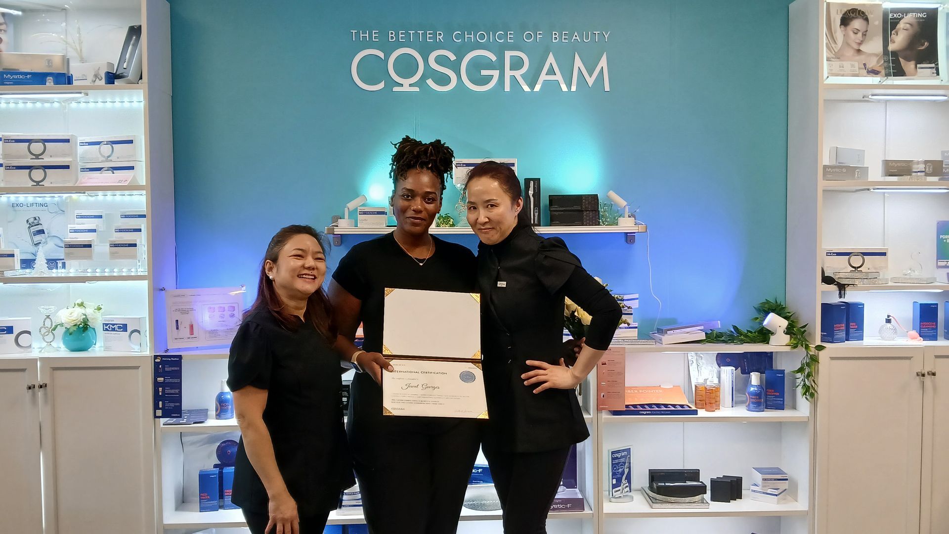 Three women pose in a medical spa, holding a certificate. The teal wall behind them has the clinic's name, Cosgram.
