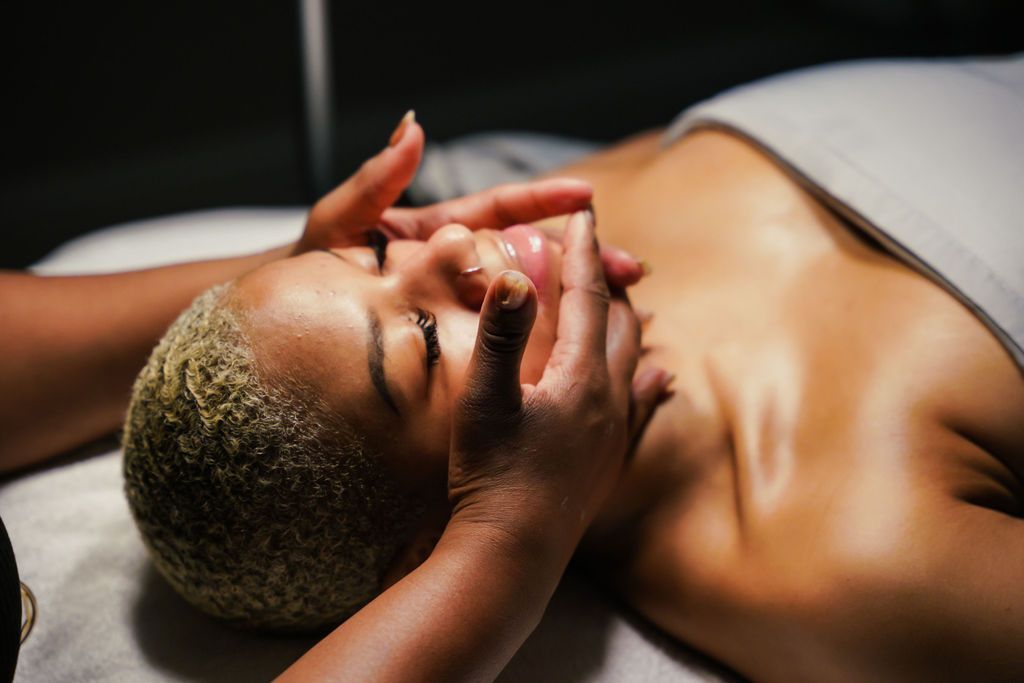 A person lying down receives a facial massage from an aesthetician in a softly lit, professional setting.