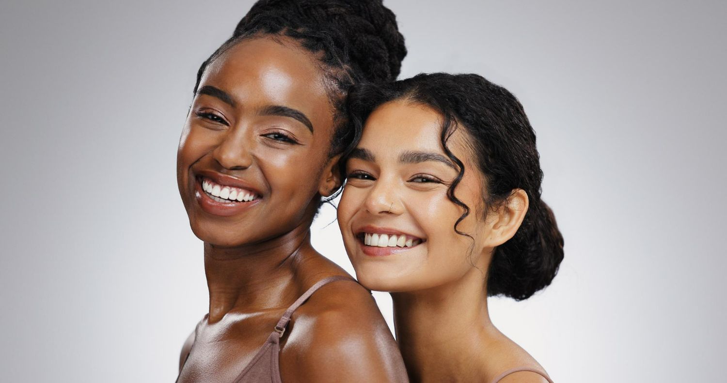 Two people smiling warmly at the camera against a plain, light gray background.