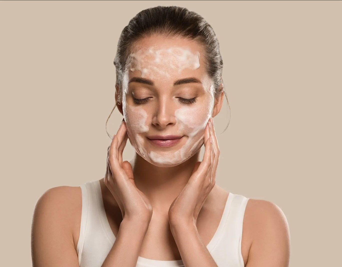 A woman is washing her face with soap foam.