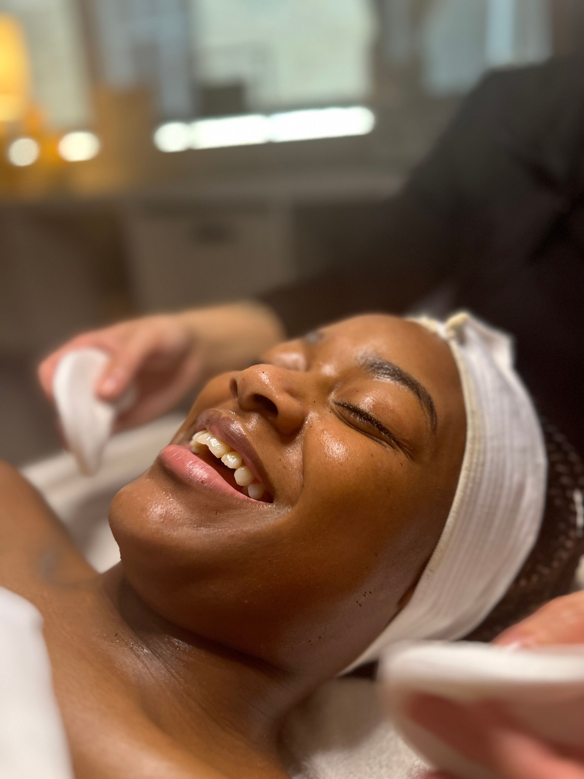 A woman is smiling while getting a facial treatment at a spa.