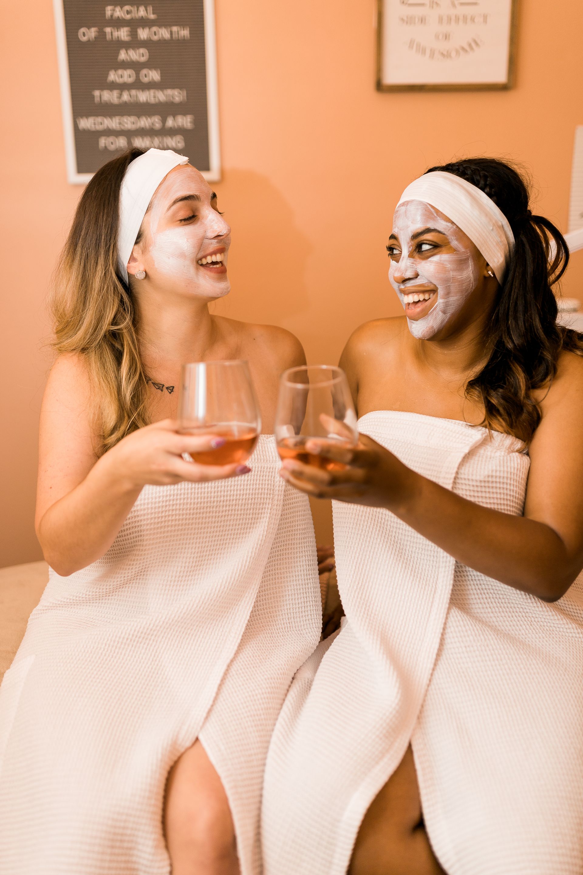 Two women in bathrobes with towels wrapped around their heads are sitting next to each other on a bed.