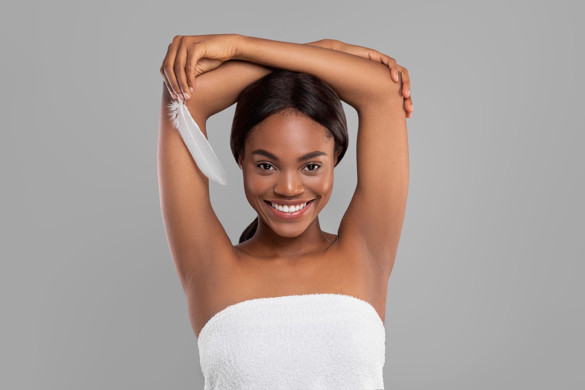 A woman wrapped in a towel is applying lotion to her armpits.