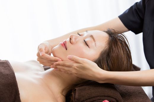 Woman receiving facial massage at a spa, with hands on her face.