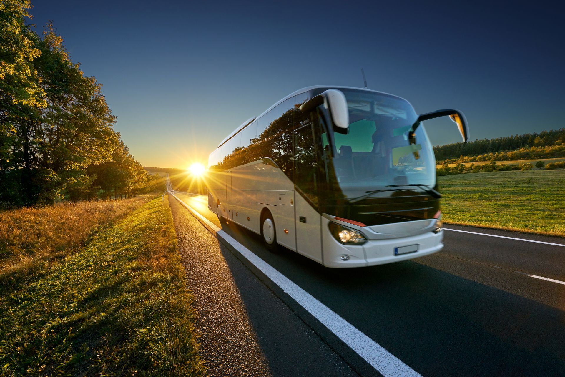 White tour bus on a road at sunrise, with open door and green landscape.