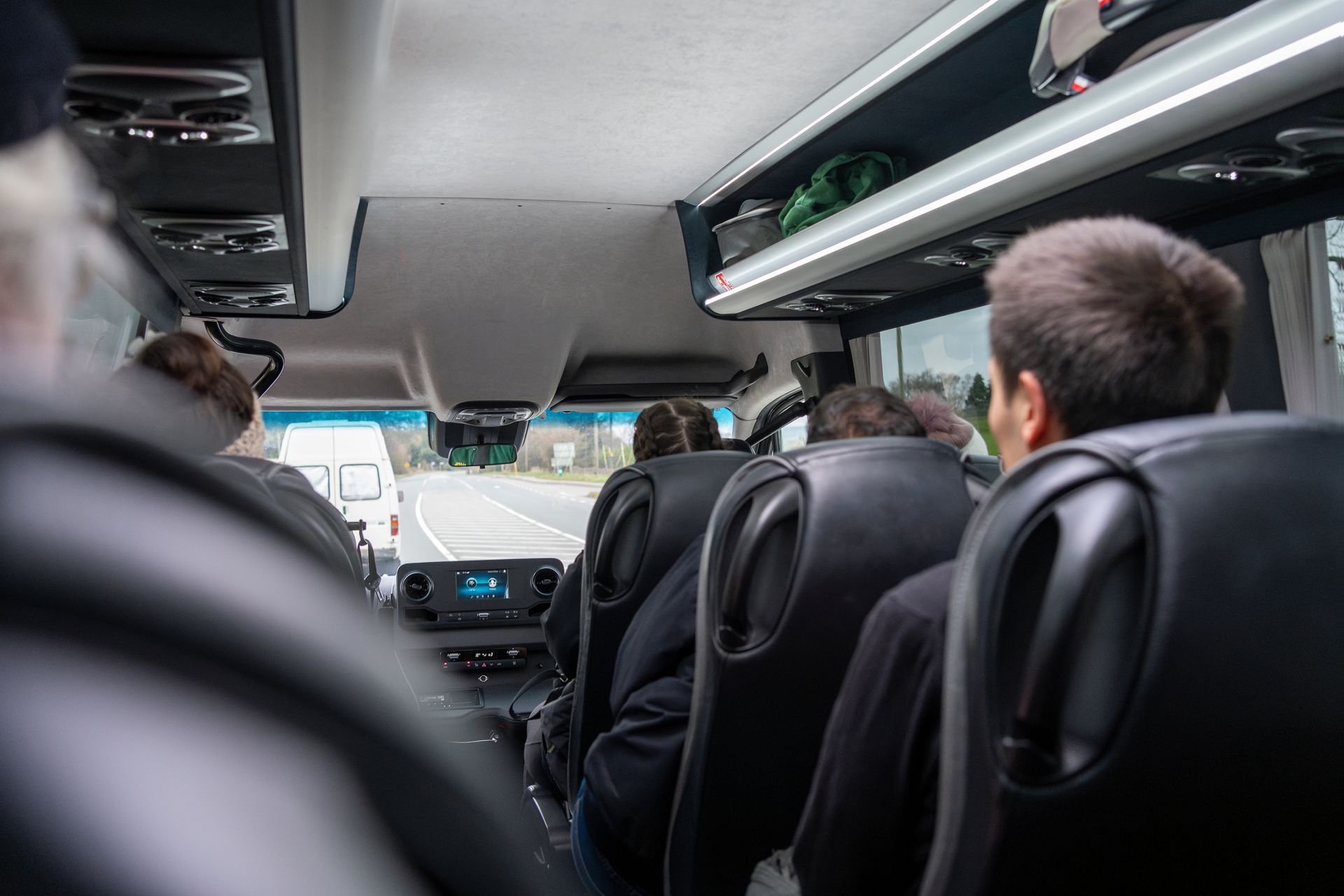 Interior view of a bus with passengers. Some are looking forward, others have their backs to the camera.