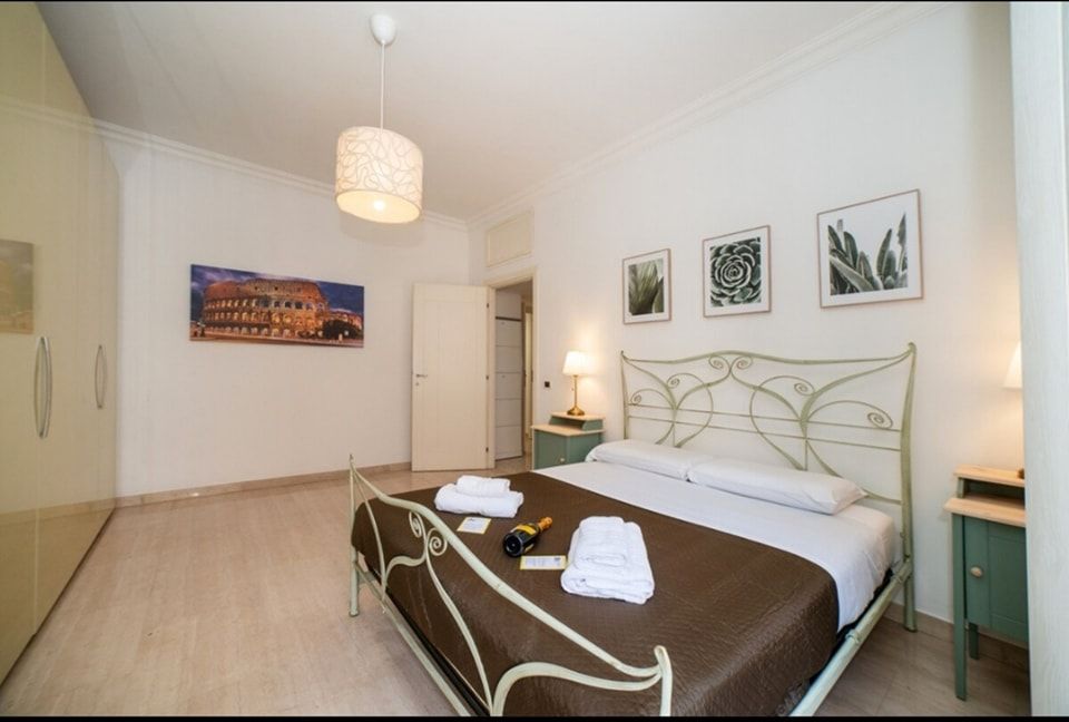 Camera da letto con letto bianco, quadri botanici incorniciati, un quadro del Colosseo e armadio beige.