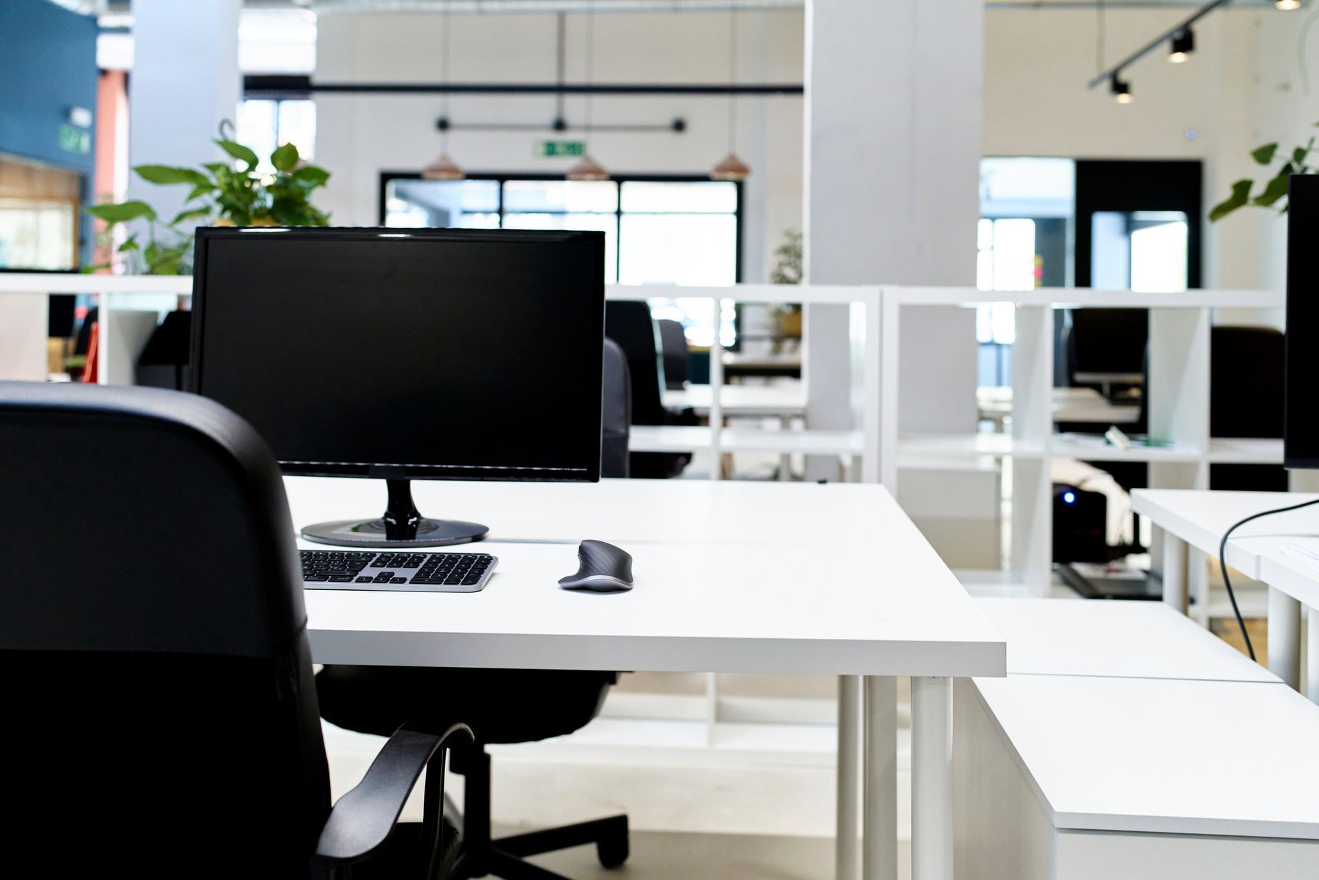 Scrivania bianca con computer, tastiera, mouse e sedia da ufficio in un ufficio open space.