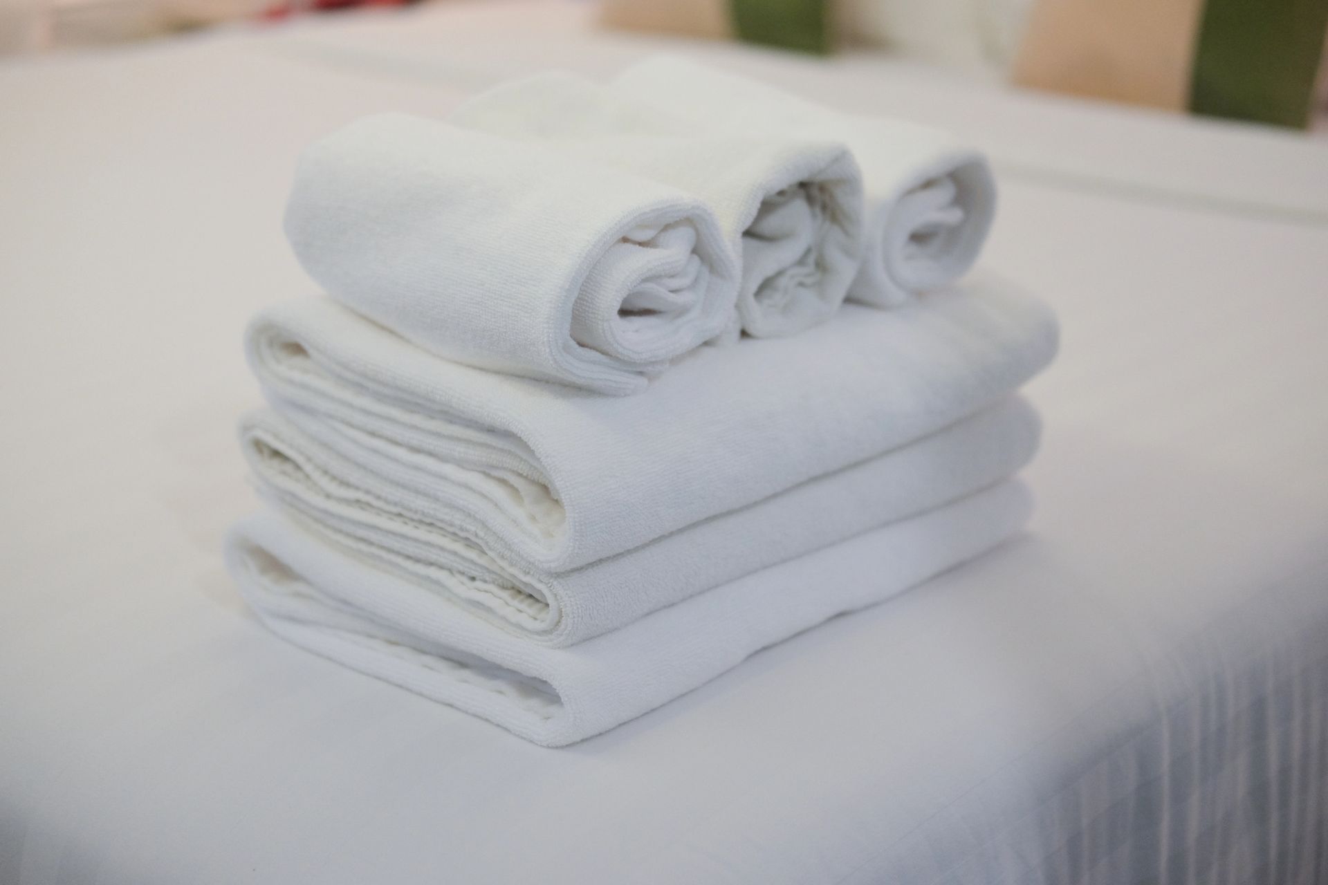 Pila di asciugamani bianchi piegati, con tre asciugamani arrotolati sopra.