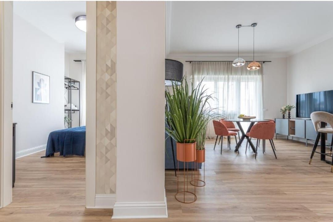 L'interno di un appartamento moderno con pavimenti in legno chiaro e pareti bianche. Sono visibili una camera da letto, una zona pranzo e un soggiorno.