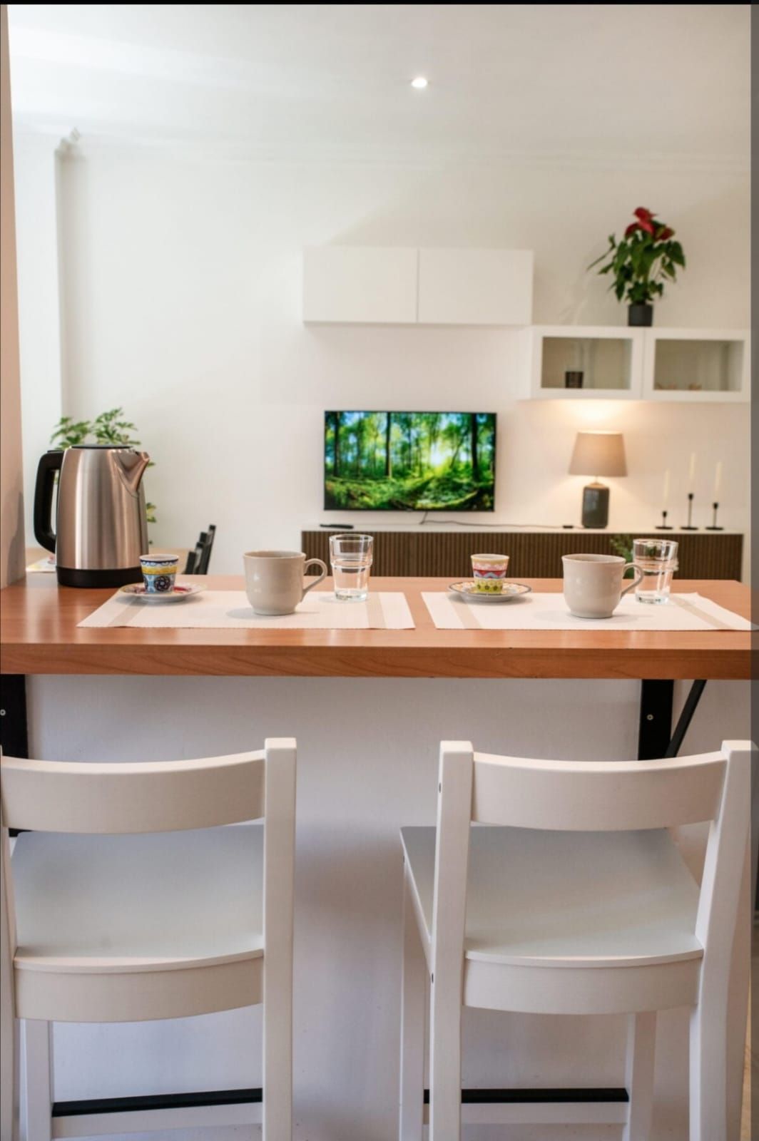 Una piccola cucina moderna con un bancone per la colazione, due sedie e una TV montata.