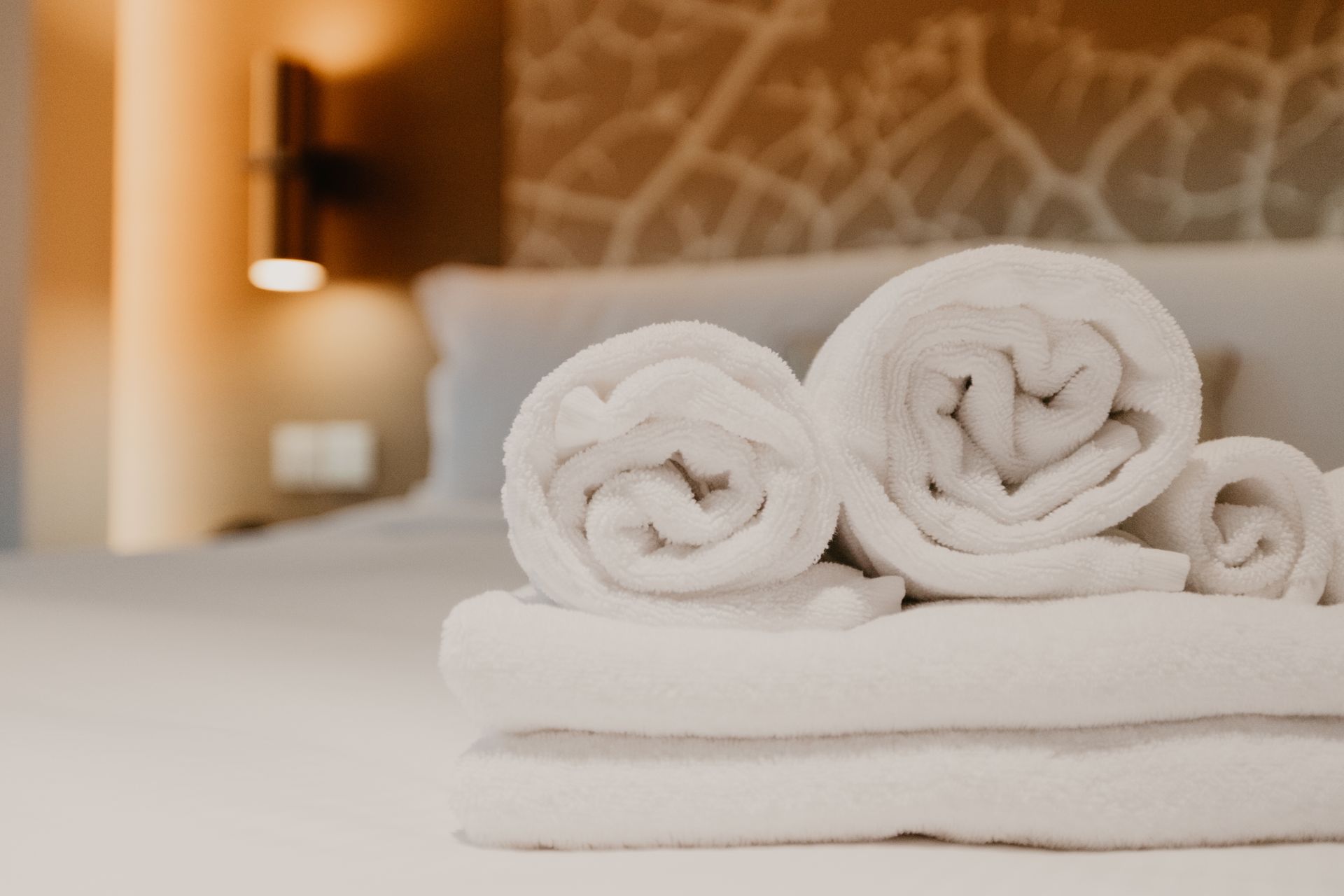 Asciugamani bianchi arrotolati ordinatamente disposti su un letto in una stanza d'albergo.