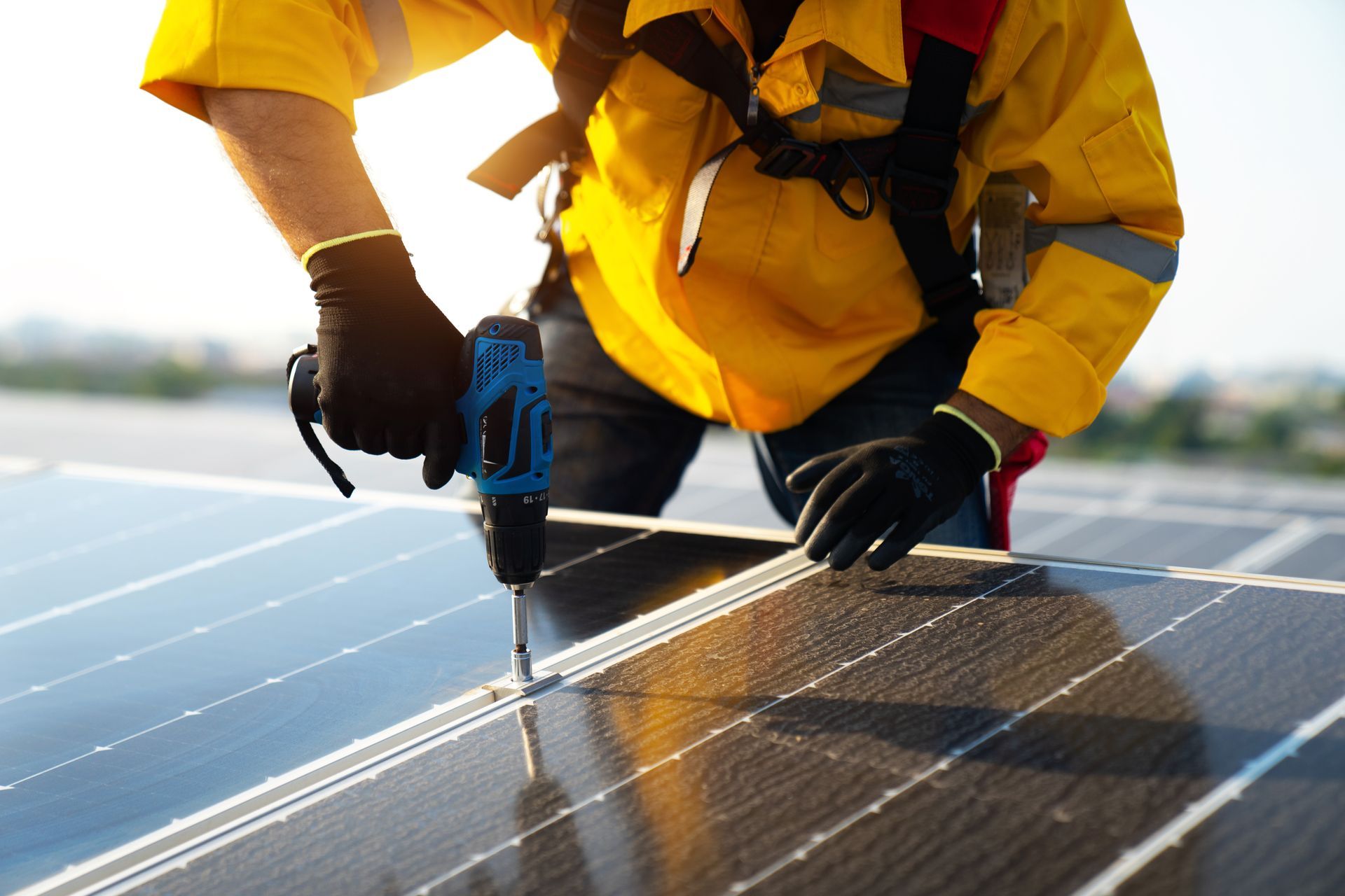 Person in yellow work clothes installing solar panels with a drill on a rooftop.