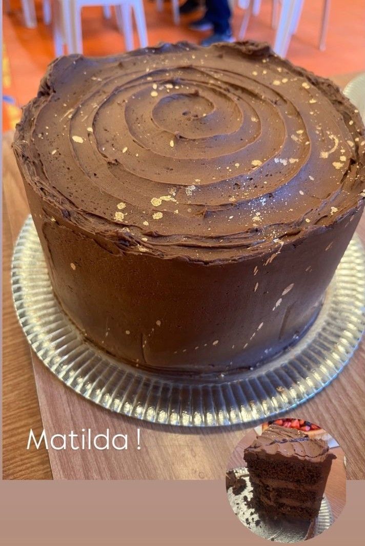 Pastel de chocolate, Matilda, en bandeja de plata, con chispas doradas y una pequeña rebanada de pastel.