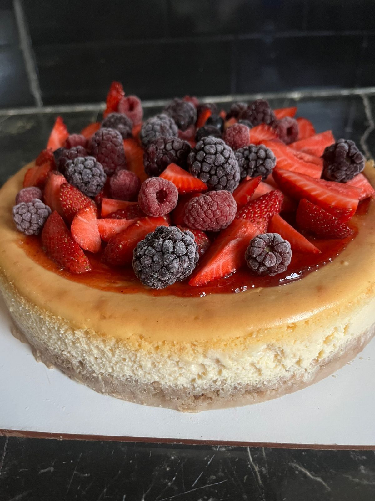 Tarta de queso cubierta con fresas, frambuesas y moras sobre una superficie blanca.