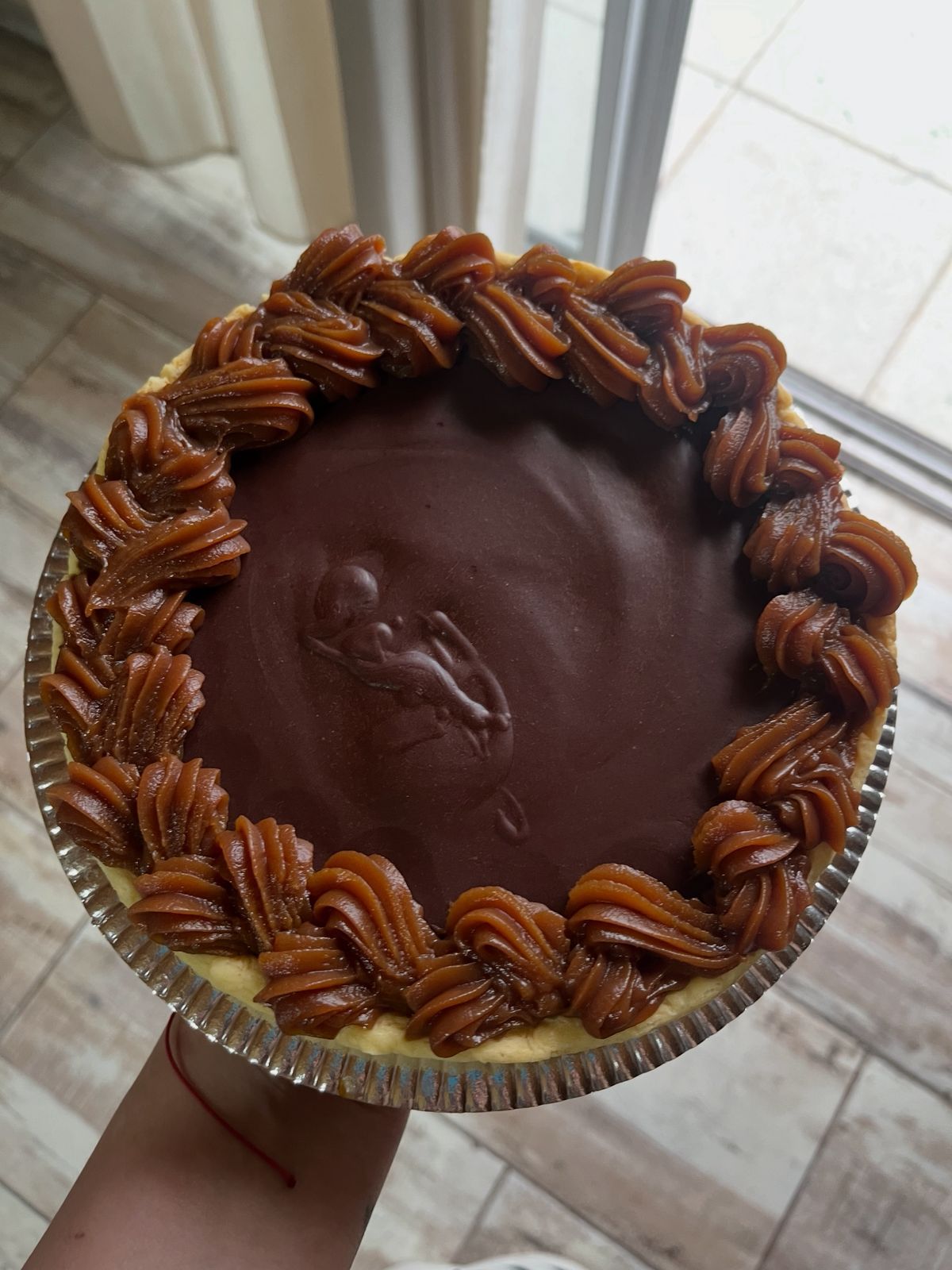 Pastel de chocolate con borde de caramelo, apoyado contra una ventana.