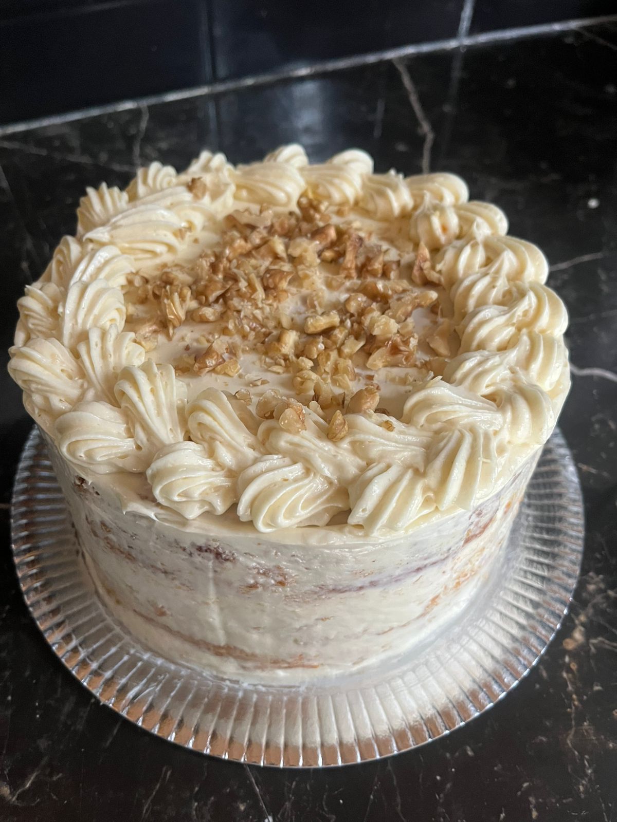 Pastel de zanahoria redondo con glaseado de queso crema, cubierto con nueces, sobre un plato de vidrio.