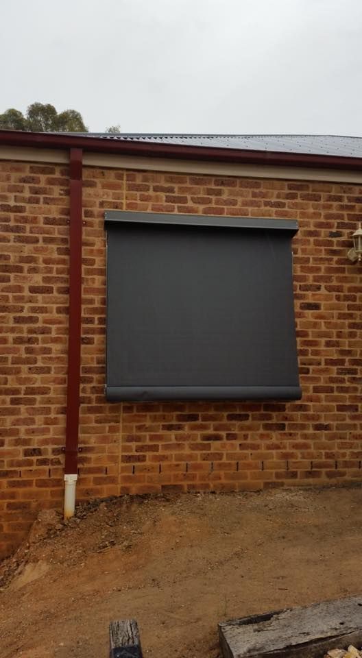 A Brick Wall With A Window With A Black Blind On It — Spring Crest Blinds, Awnings & Security Doors in Shepparton, VIC
