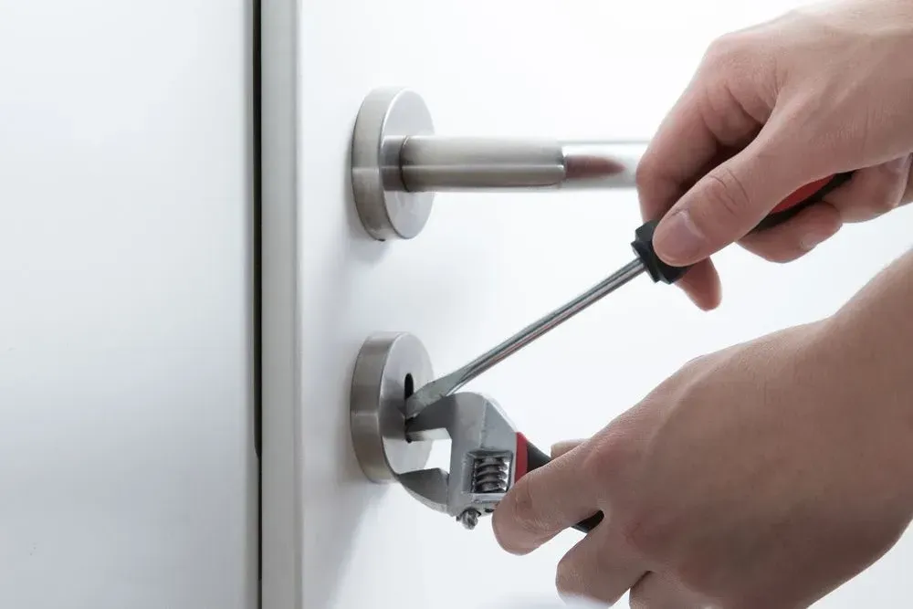 A Person Is Fixing A Door With A Wrench And Screwdriver — Spring Crest Blinds, Awnings & Security Doors in Shepparton, VIC 