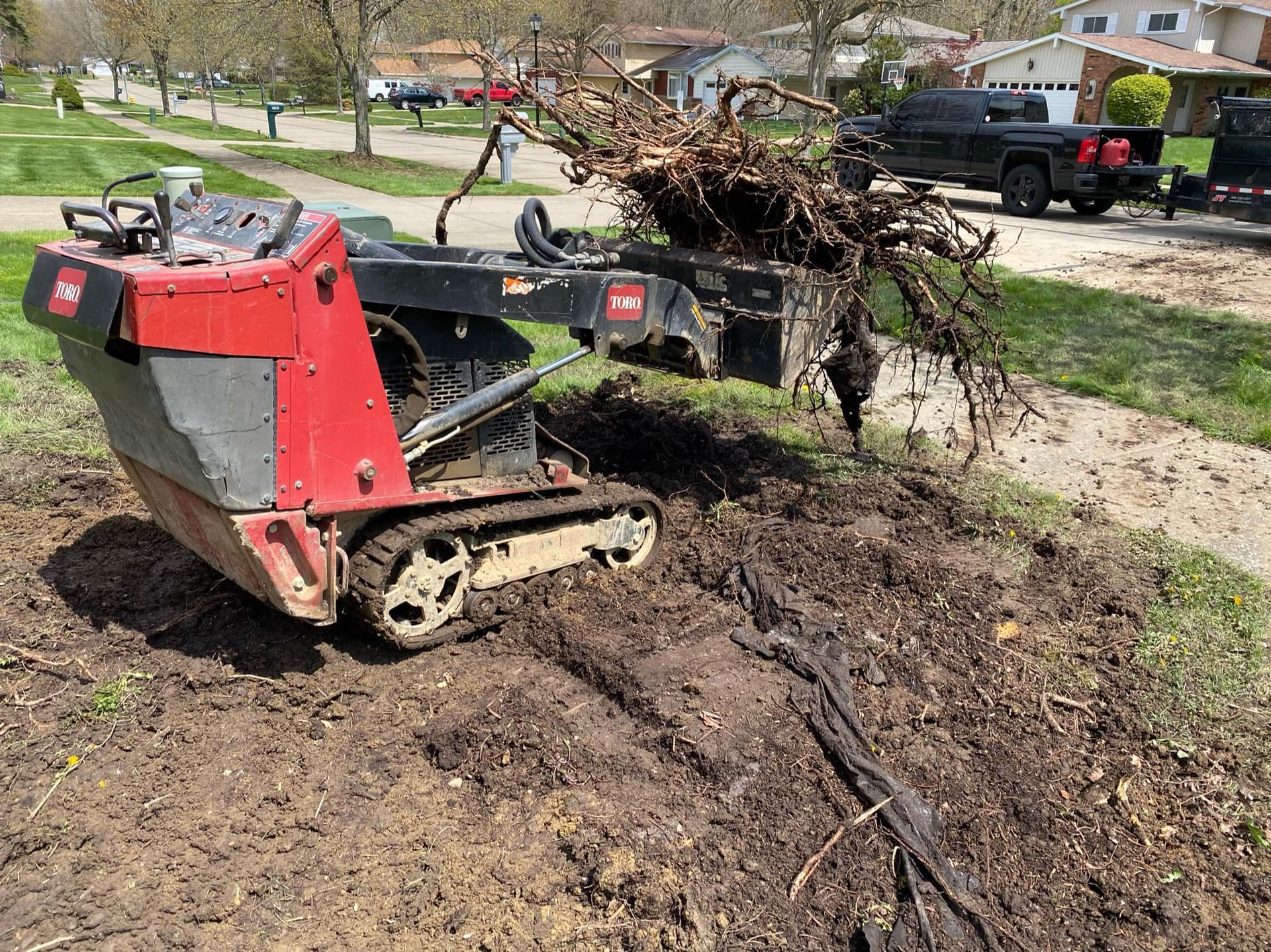 A red and black tractor is sitting in the dirt next to a truck.