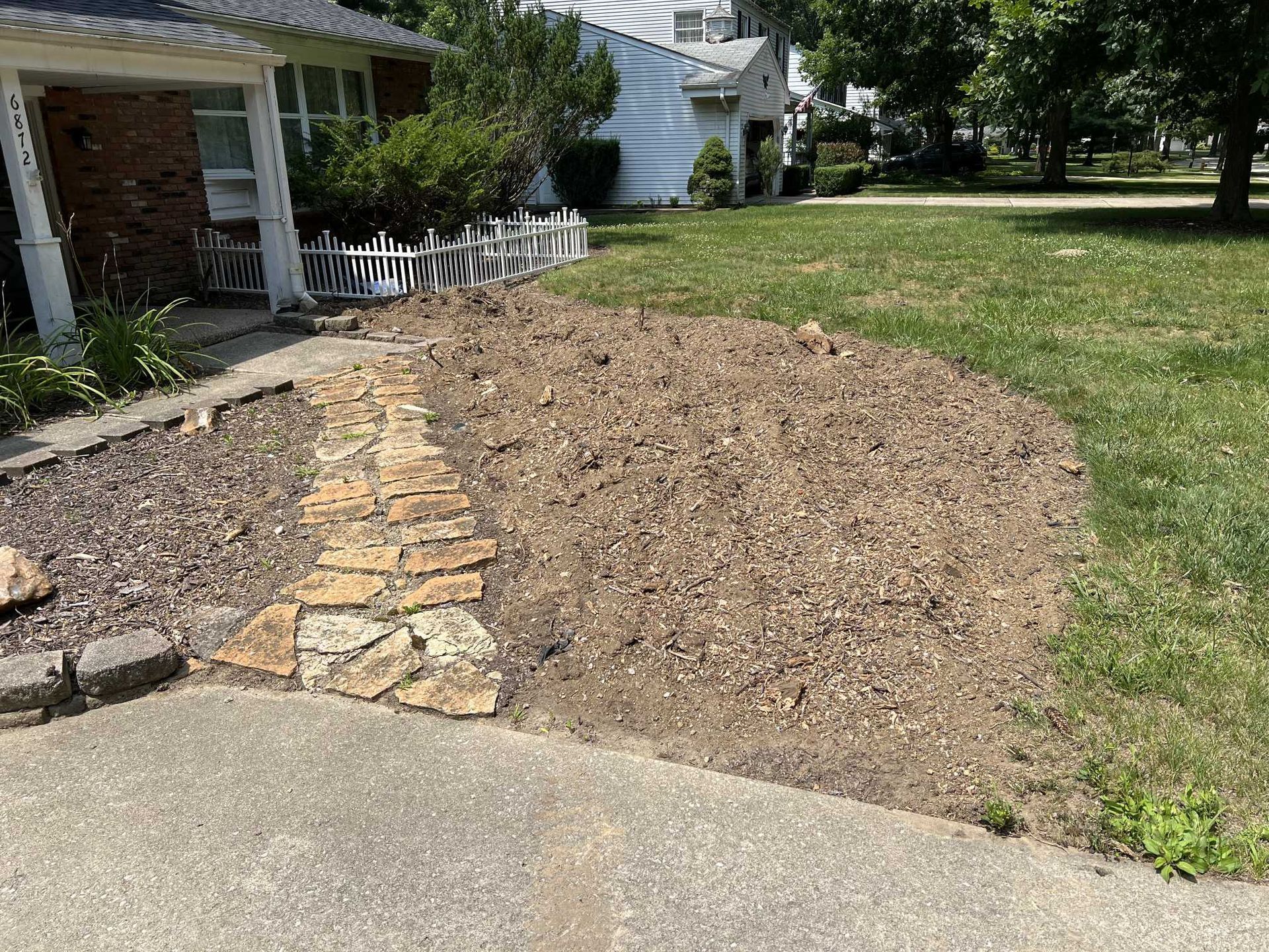 A house with a stone walkway leading to it and a large pile of dirt in front of it.