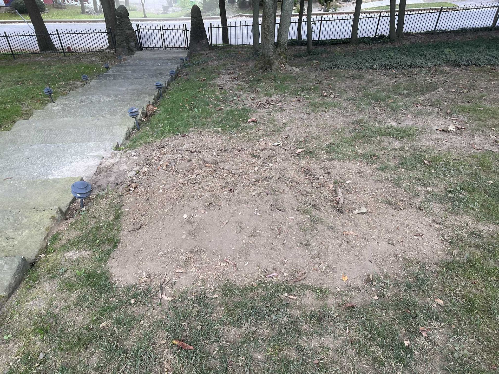 There is a dirt area in the middle of the grass next to a sidewalk.