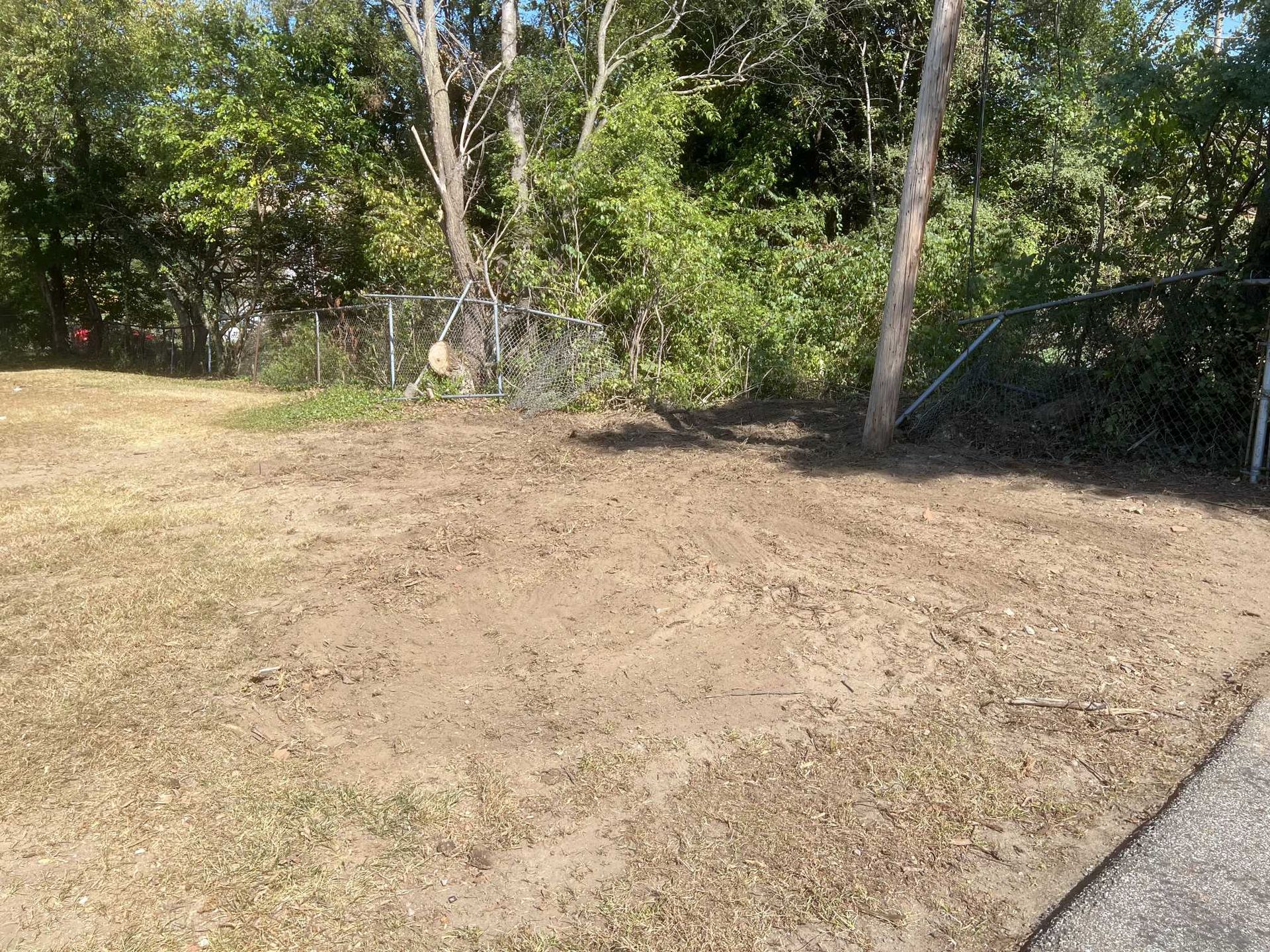 A dirt field with a fence and trees in the background.