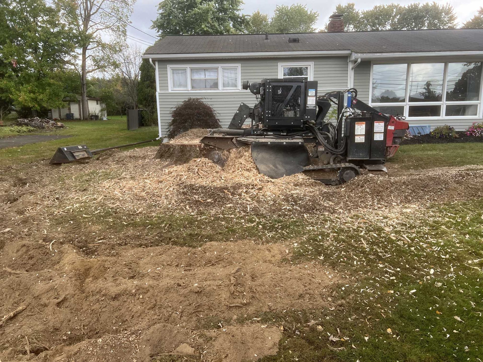 A tractor is cutting a tree stump in front of a house.